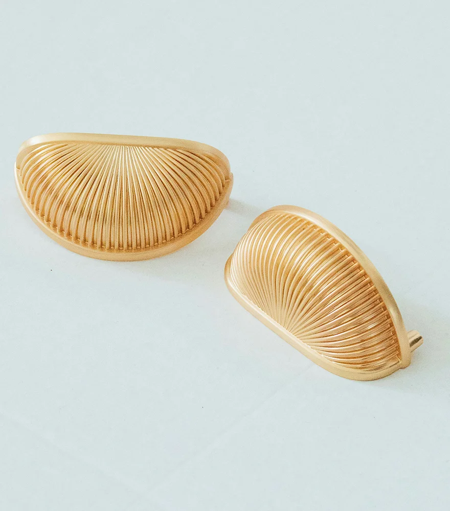 Gold earrings placed on a pale blue surface with unwanted background and shadows.