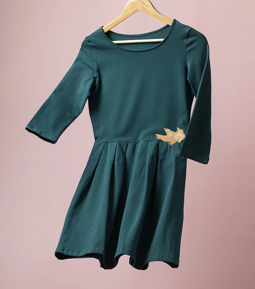 Green dress hanging on a wooden hanger with visible leaf decoration and background.