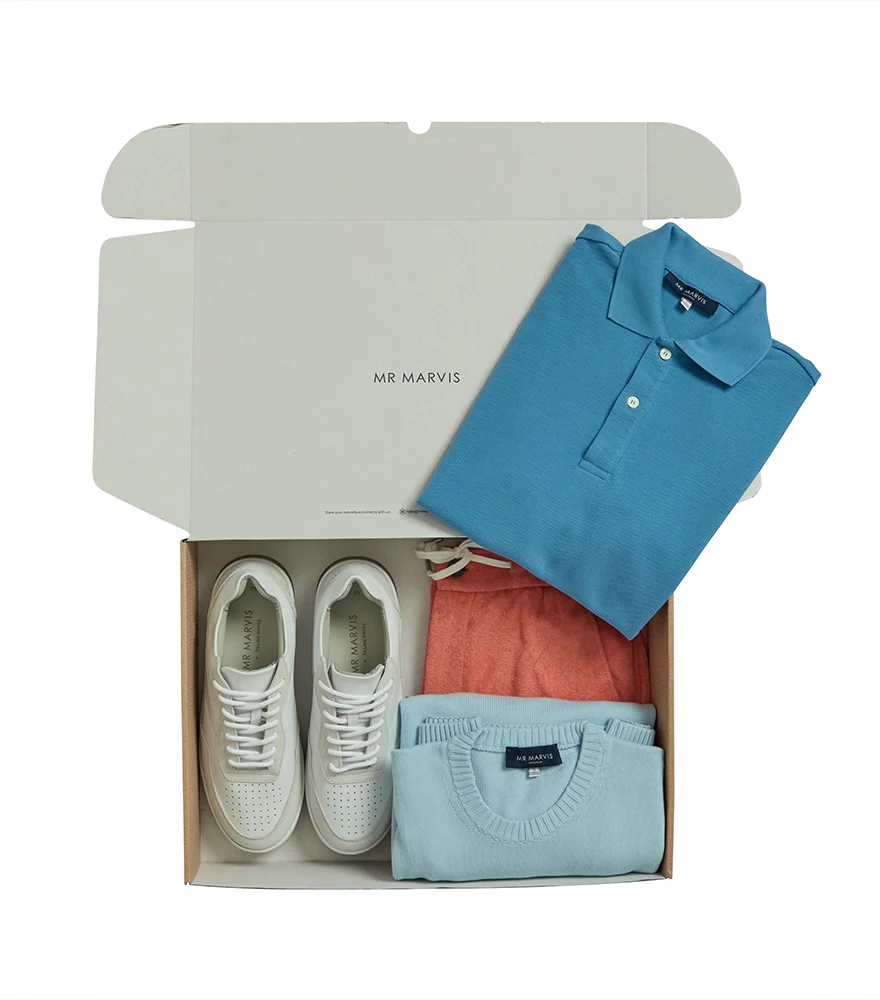 Box of folded clothing and shoes isolated on a white background.