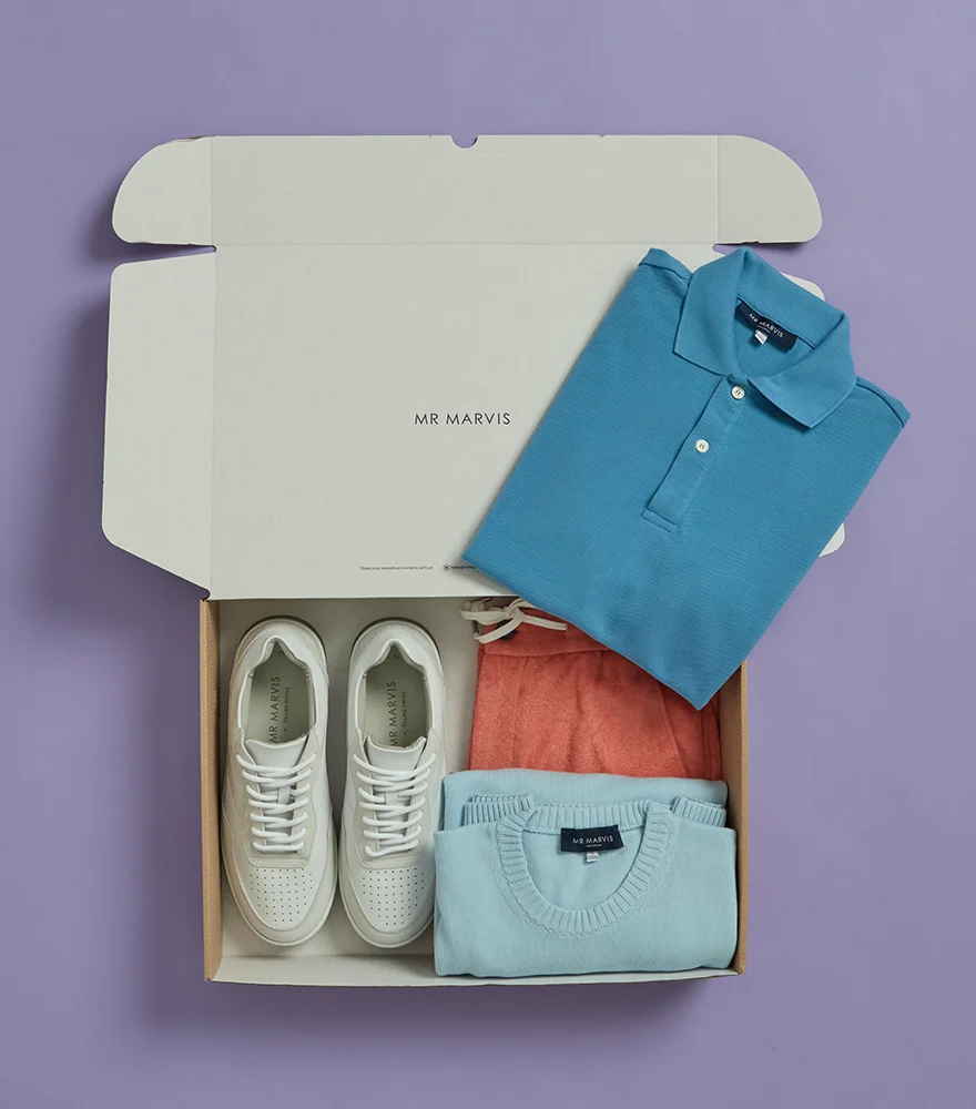 Clothing and footwear packaged in a box photographed on a purple background.