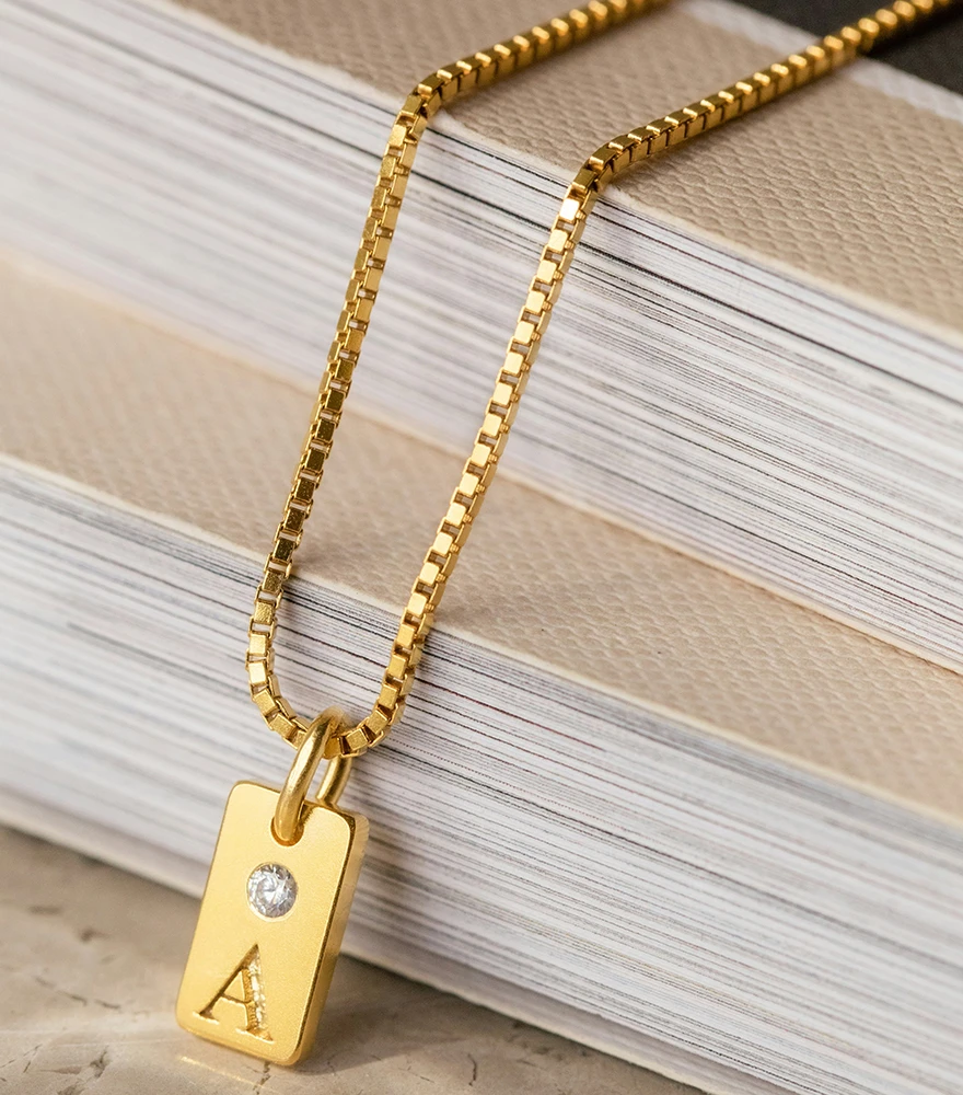 Gold necklace with diamond pendant displayed on textured book surface.