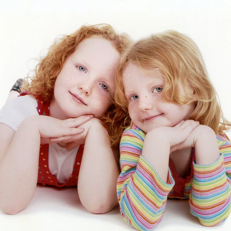 Two young red-haired girls smiling and lying close together in a professionally restored photograph.