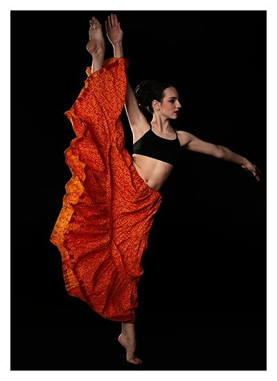 Female contemporary dancer in dramatic pose wearing black top and flowing orange skirt.