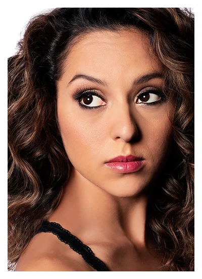 Woman with curly hair, dramatic eye makeup, and pink lipstick looking sideways.