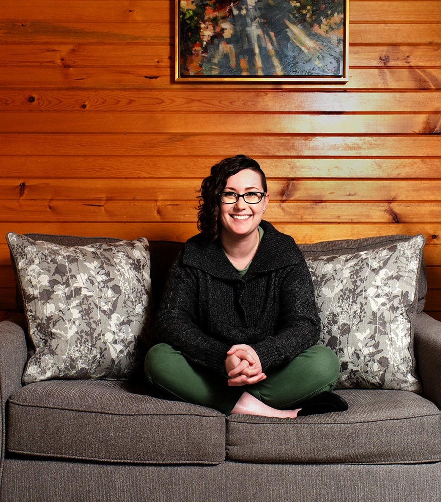 Object Removal & Additions_Before Woman seated on sofa with Framed painting wooden wall behind her.