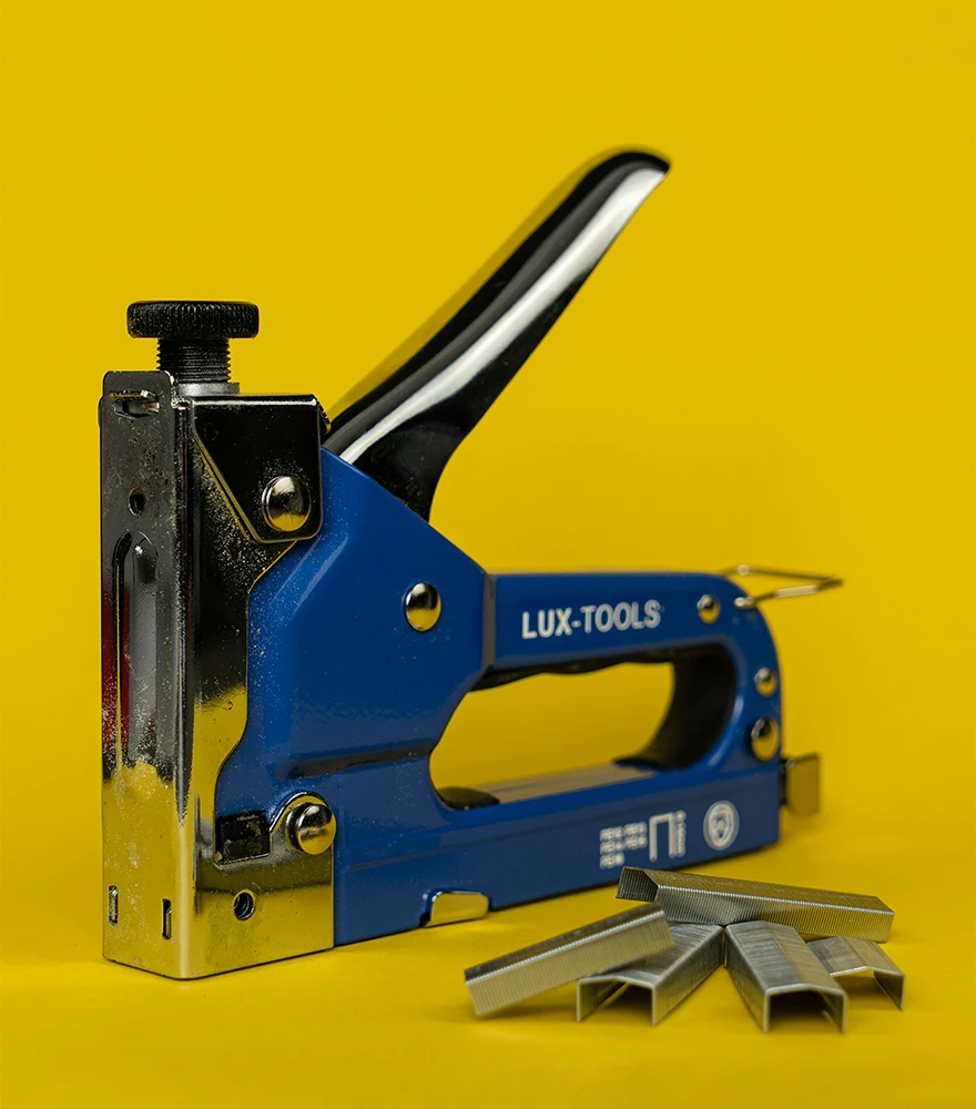Unedited photo of a Lux-Tools stapler on a yellow background with reflections and minor dust.