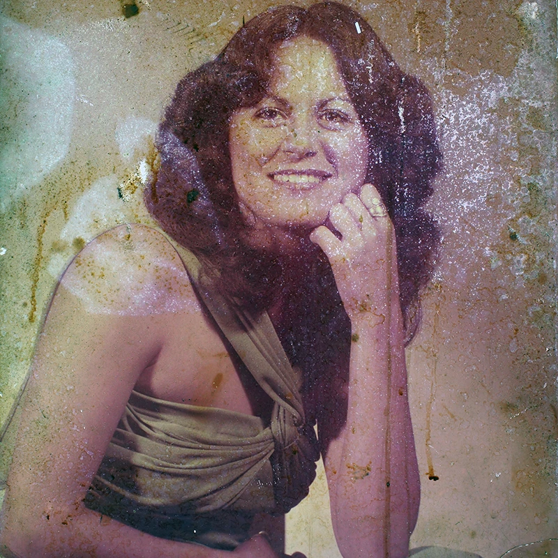 Heavily damaged and faded portrait of a woman, showing water stains, discoloration, and scratches.